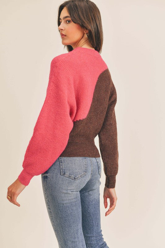 Back view of a woman with wearing jeans, she is also wearing a half bright pink, half brown, semi cropped length, balloon sleeve sweater.