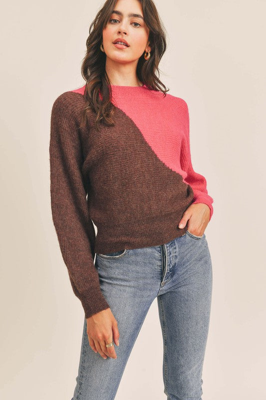 Woman facing forward with wearing jeans with one hand in the front pocket, she is also wearing a half bright pink, half brown, semi cropped length, balloon sleeve sweater.