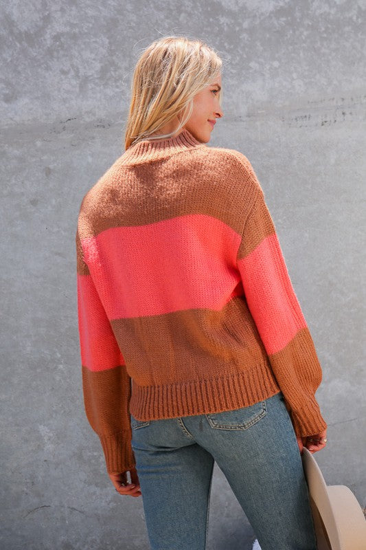 Woman wearing a cidar colored sweater with a large bright coral stripe across the middle, balloon sleeves, mock neck, ribbed at cuffs and bottom. Rear view of item.