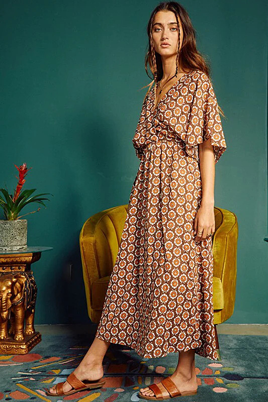 A woman wearing a kimono style midi dress in brown block print. This is a side view of the item.
