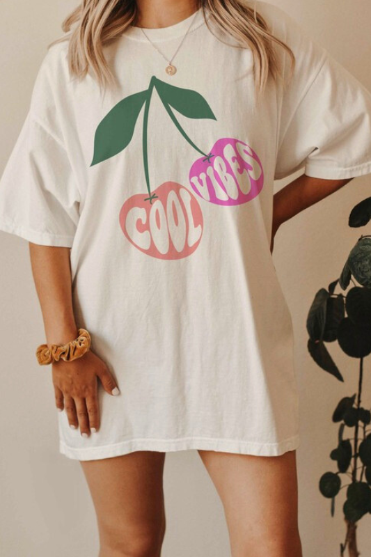 Cool vibes graphic tee with peach and pink cherries, worn by a woman from the front.