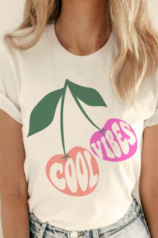 Cool vibes graphic tee with peach and pink cherries, worn by a woman from the front.