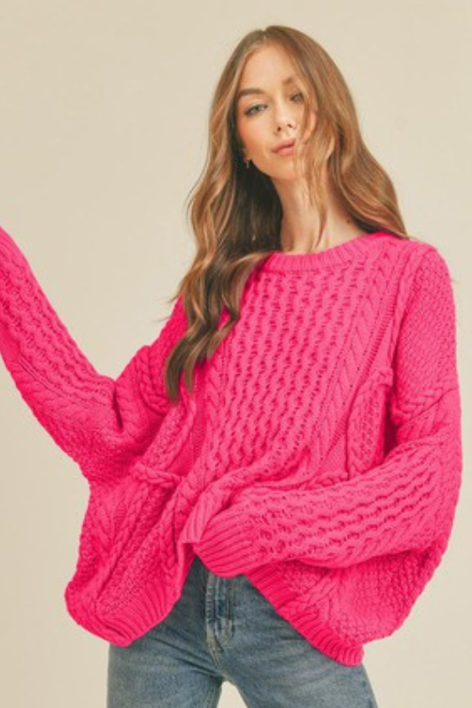 Woman wearing a bright pink oversized, drop shoulder, cable knit sweater.